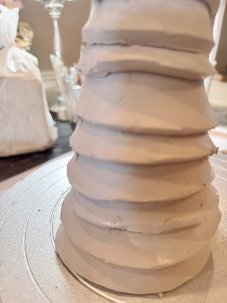 A close-up of a gray, layered, and textured cylindrical sculpture or object on a metallic circular base.