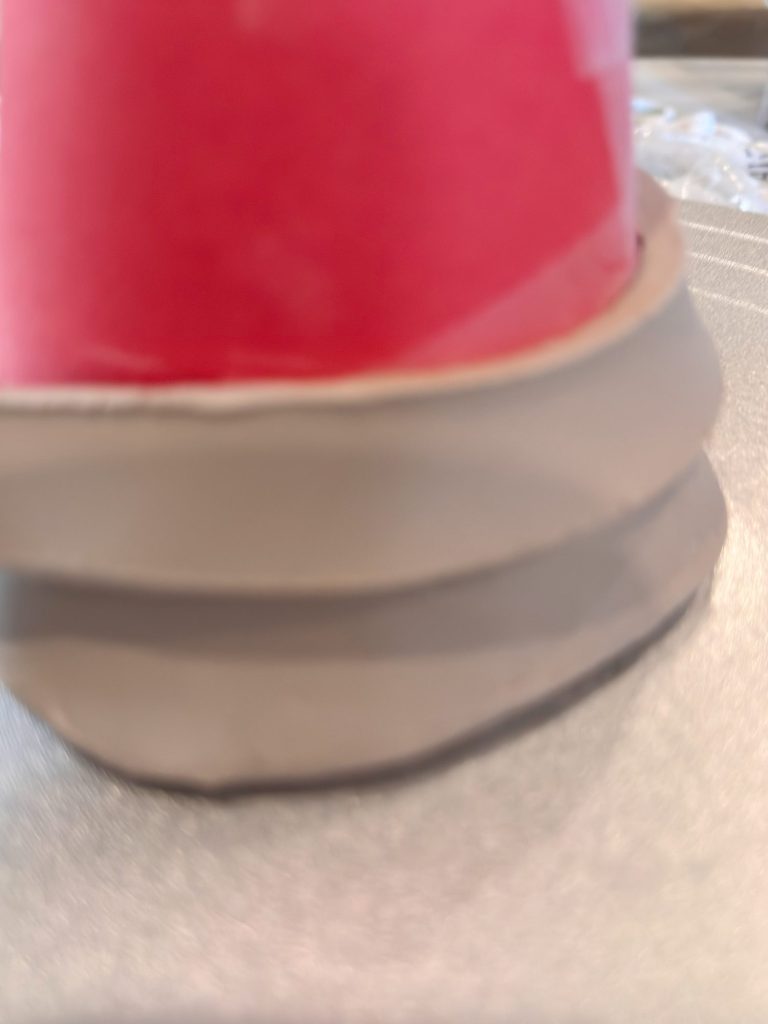 A close-up image of the base of a red cup with a beige, textured silicone or rubber grip, positioned on a metallic surface.