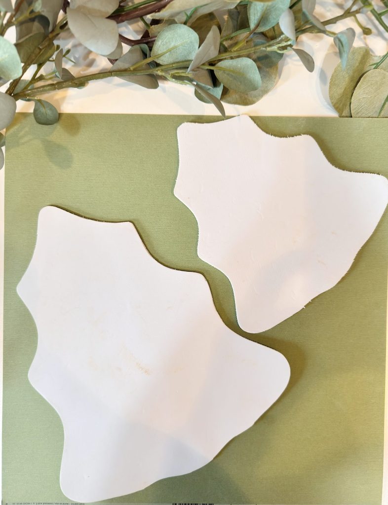 Two irregularly shaped, white ceramic plates are placed on a green surface with eucalyptus leaves in the background.