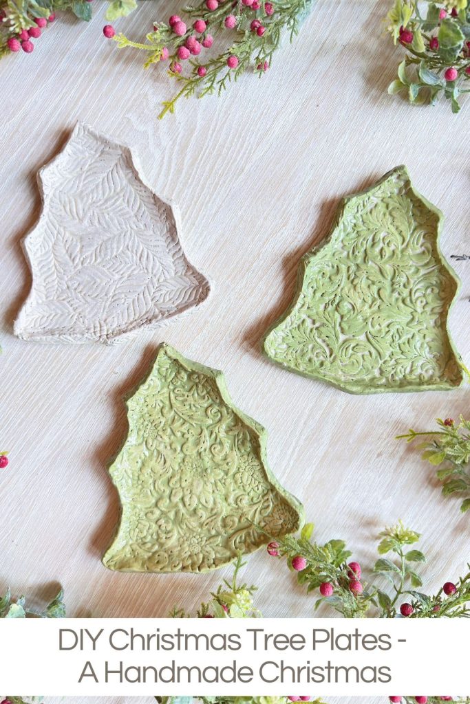 Three textured ceramic plates shaped like Christmas trees, two green and one white, are displayed on a light wooden surface with festive greenery and red berries nearby.