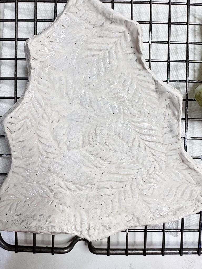 A glossy ceramic slab with an embossed fern leaf pattern rests on a metal cooling rack.