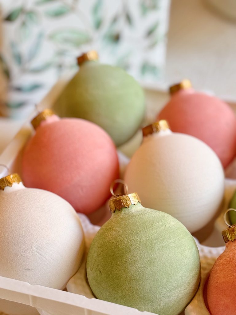 A close-up of pastel-colored Christmas ornaments in pink, green, and white, arranged in a plastic tray.