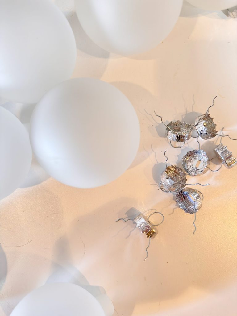 Frosted white glass ornaments and several detached silver ornament hangers are scattered on a white surface.
