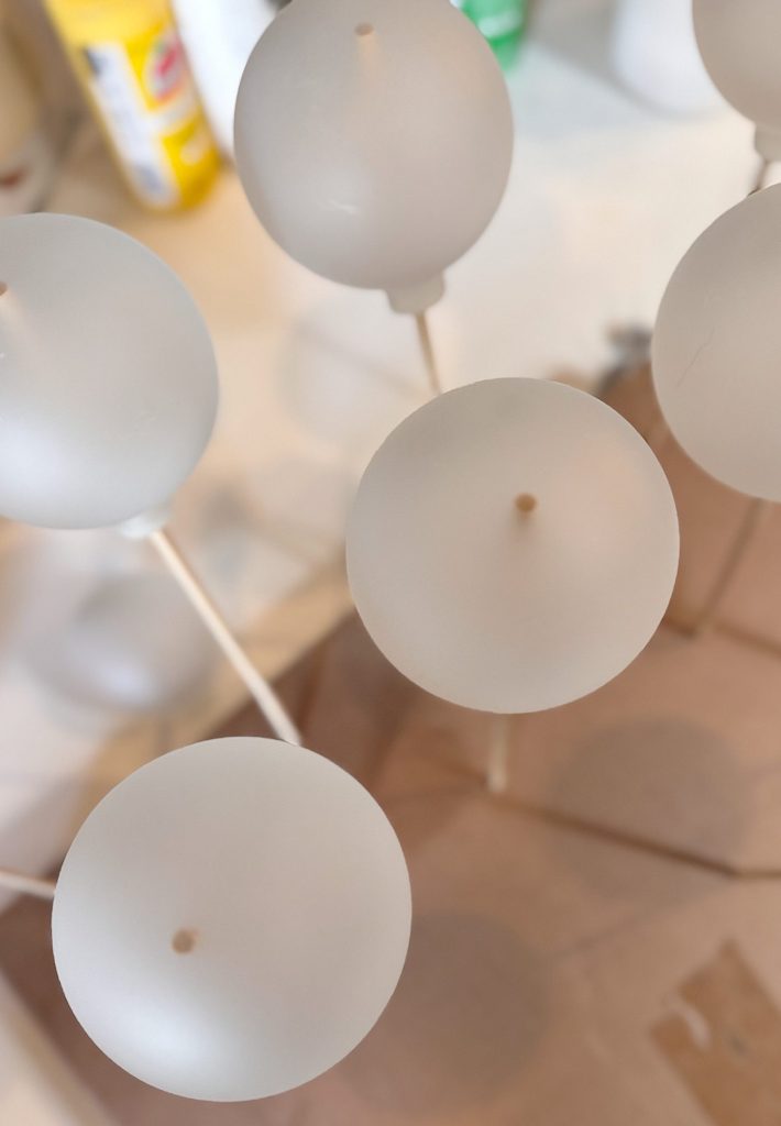 Frosted spherical objects with holes in the center are mounted on sticks and positioned upright on a cardboard surface.
