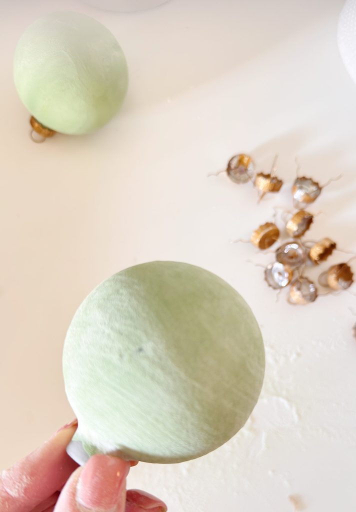 A hand holds a pale green balloon; several gold glittered acorn caps are scattered on a white surface in the background.
