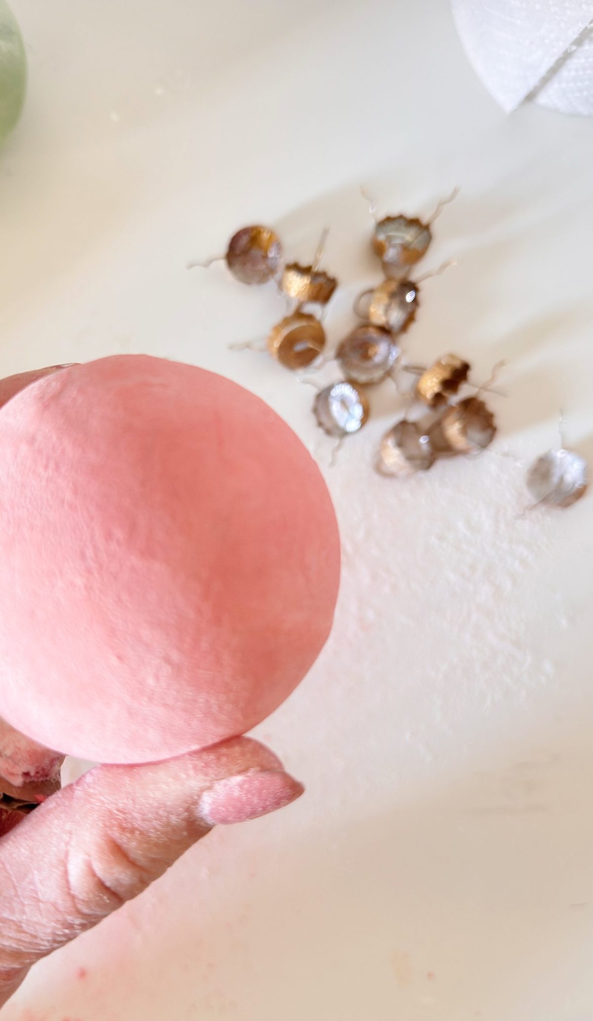 A hand holds a round, pink mochi. Several empty brown and silver cupcake liners are scattered on a white surface in the background.