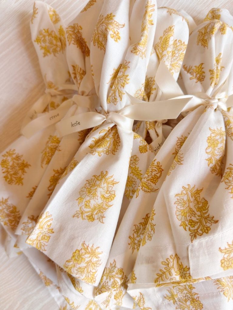 White fabric bags with a yellow floral pattern, tied with cream-colored ribbons, are arranged on a light surface.