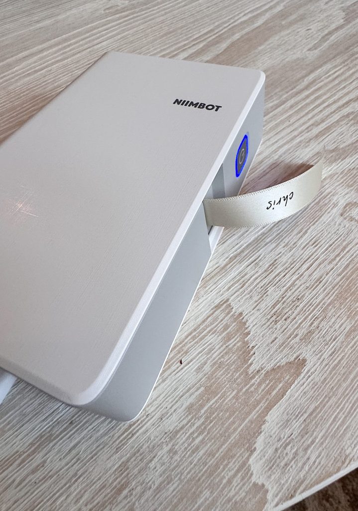 A NIIMBOT label maker sits on a light wood surface, dispensing a label with the text "CAT-5" printed on it.