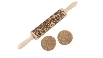 A wooden rolling pin with engraved floral patterns and two round cookies imprinted with the same decorative designs.