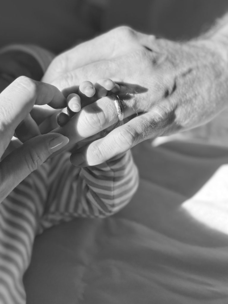 An adult hand with a ring and another adult hand gently hold a newborn baby's hand, which is dressed in striped fabric, evoking the delicate beauty of Mercury Glass Ornaments.