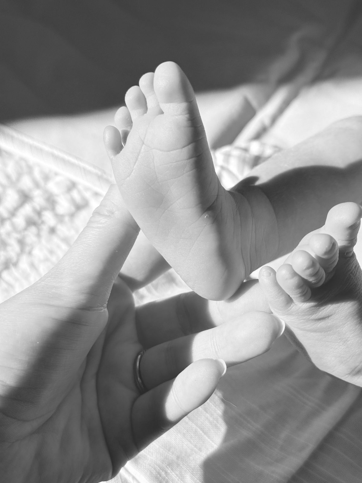 An adult hand gently touches the sole of a baby&rsquo;s foot, with another baby foot visible beside it in soft natural light, reminiscent of the delicate charm found in mercury glass ornaments.