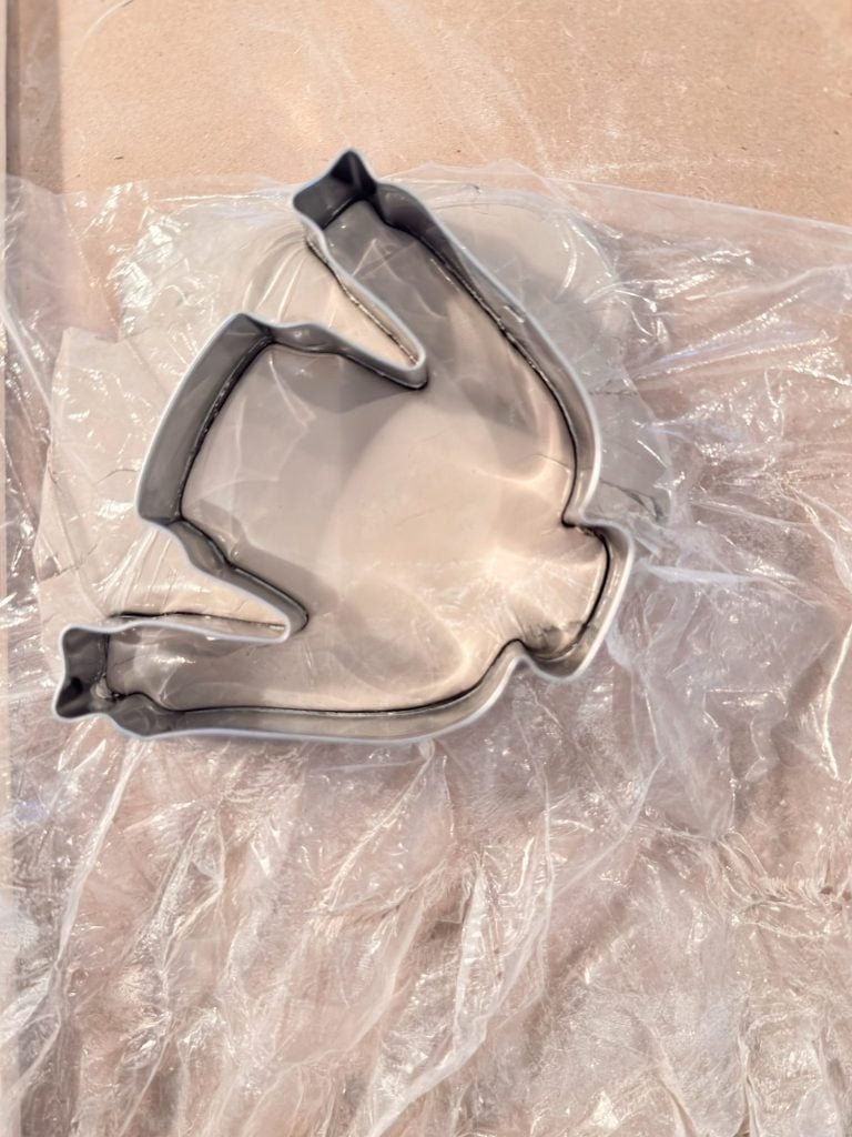 A metal bat-shaped cookie cutter rests on a sheet of crinkled clear plastic.