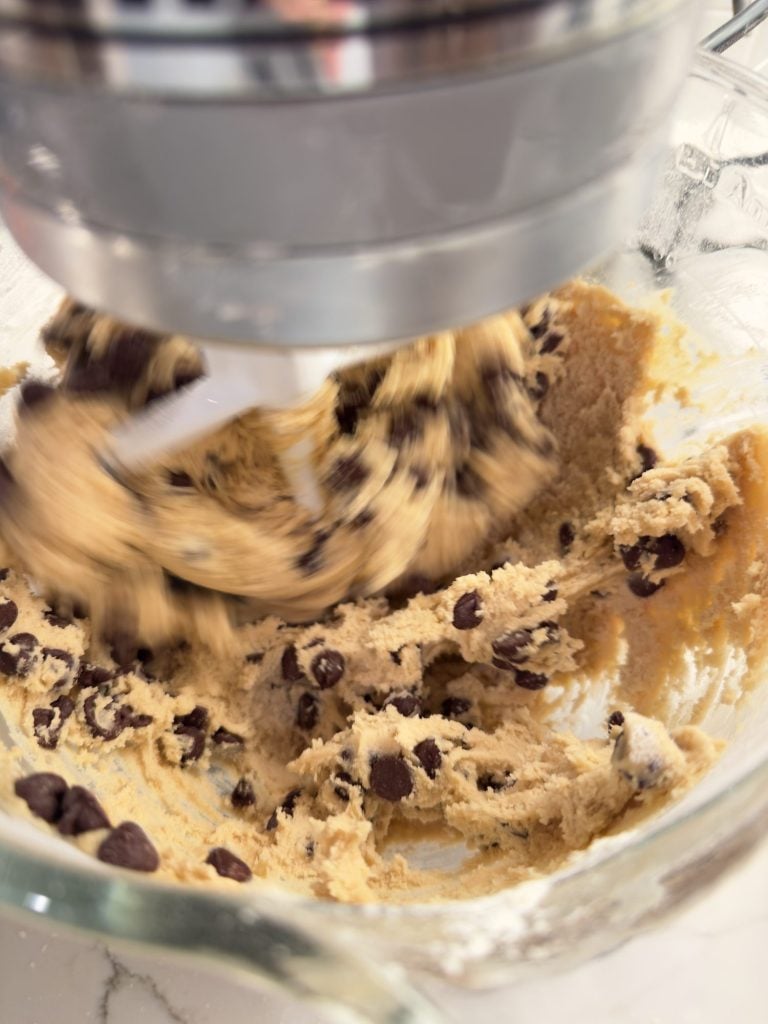 Close-up of cookie dough with chocolate chips being mixed in a stand mixer bowl.