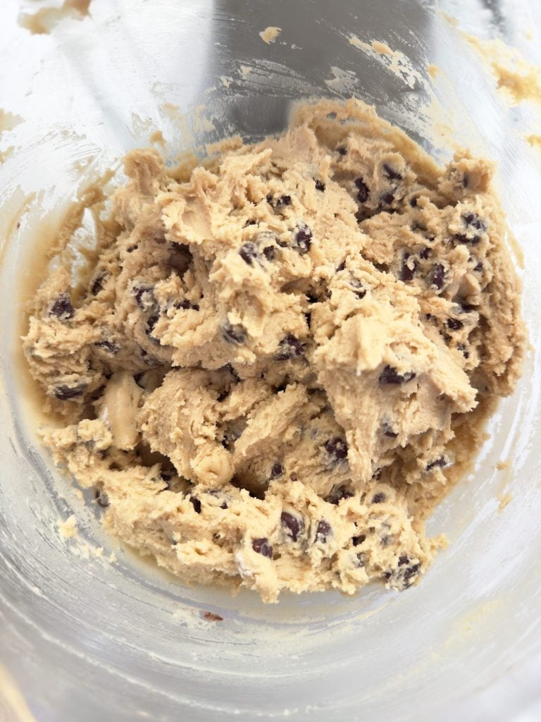 A close-up of chocolate chip cookie dough in a glass mixing bowl.