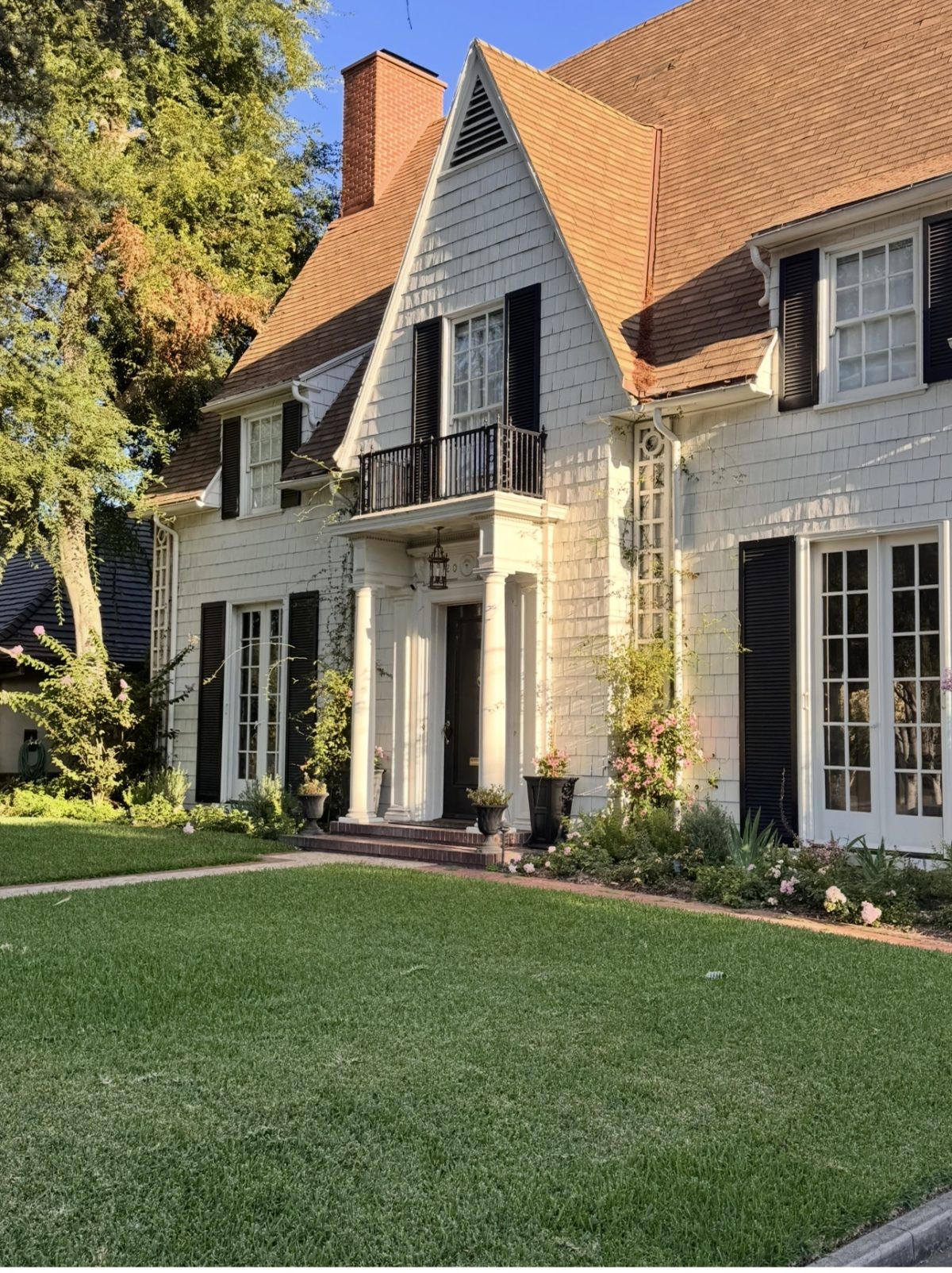 Two-story house with white siding, black shutters, gabled roof, front porch with columns, and a manicured lawn.