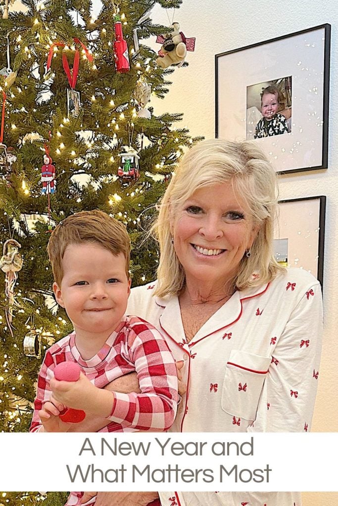 A woman and a young boy in pajamas pose in front of a decorated Christmas tree, with framed photos on the wall behind them.