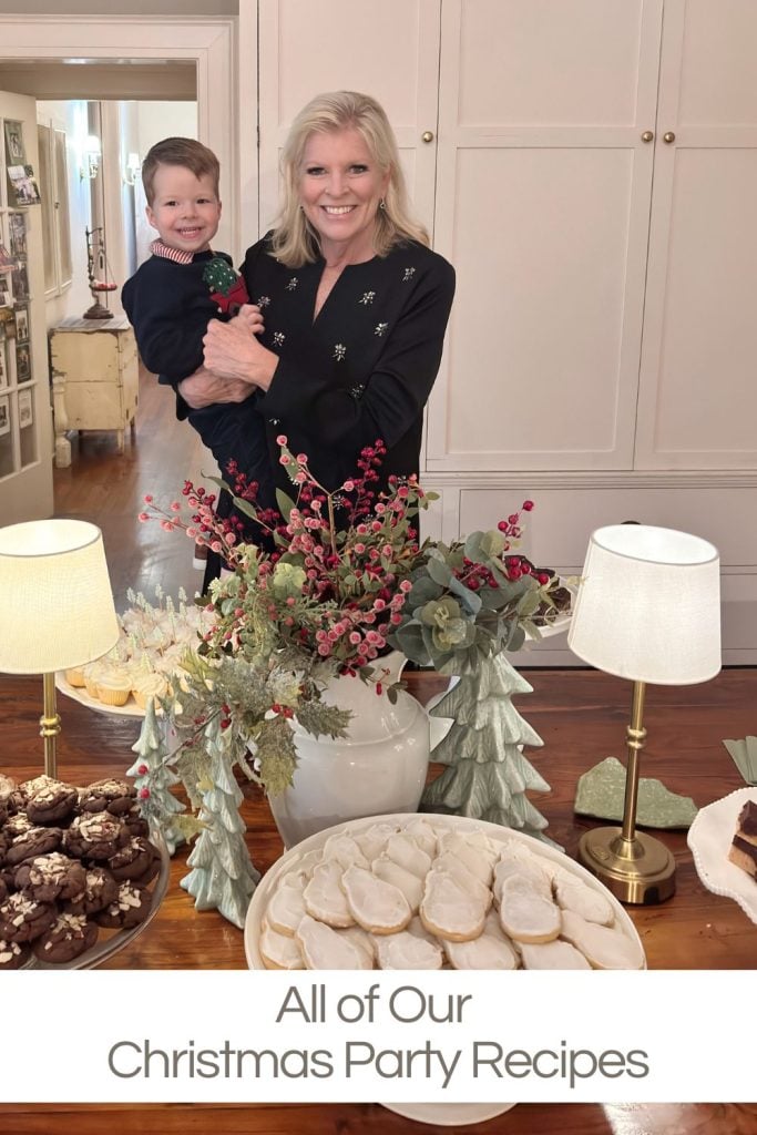 A woman holding a young child stands behind a table with assorted Christmas cookies, lamps, and festive decorations; text reads, "All of Our Christmas Party Recipes.