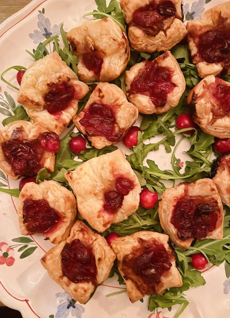 A plate of puff pastry squares topped with cranberry sauce, arranged on a bed of arugula and garnished with fresh cranberries.