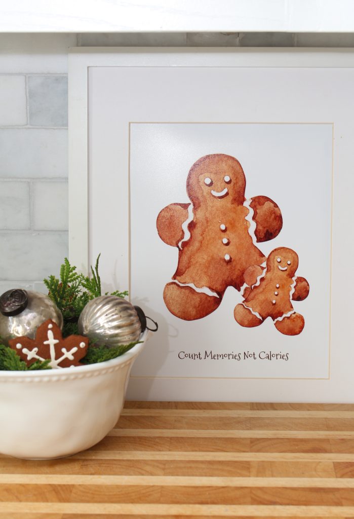 Framed illustration of two gingerbread cookies with the text "Count Memories Not Calories," next to a bowl with ornaments, greenery, and an iced gingerbread cookie.