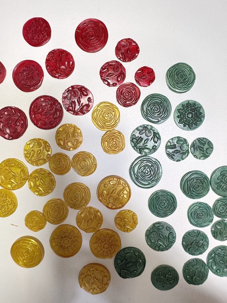 Red, yellow, and green circular wax seals with embossed floral patterns are arranged on a white surface.