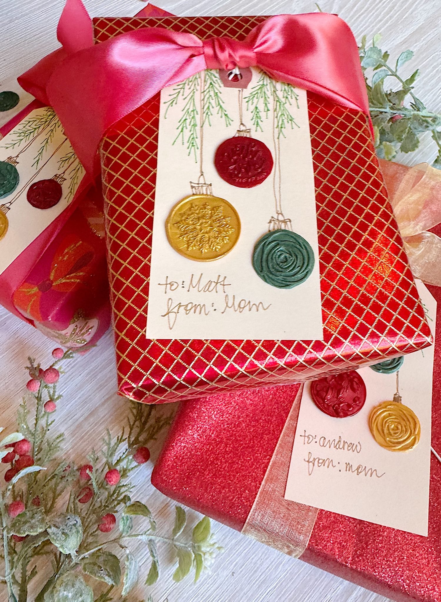 Two wrapped gifts with red and gold paper, decorated with large bows and handmade gift tags featuring wax seals and handwritten names from Mom to Matt and Andrew.