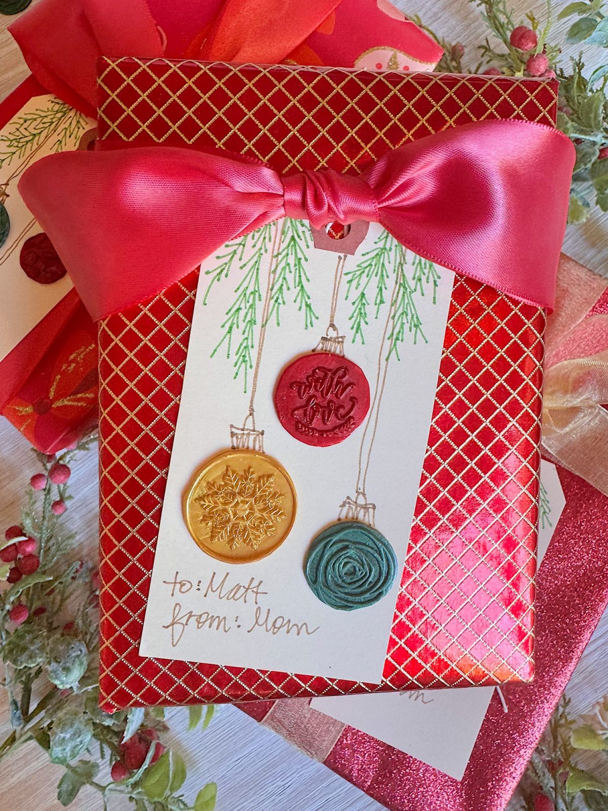 A red gift with a large pink bow and a tag decorated with three ornaments, addressed &ldquo;to: Matt from: Mom.&rdquo;.