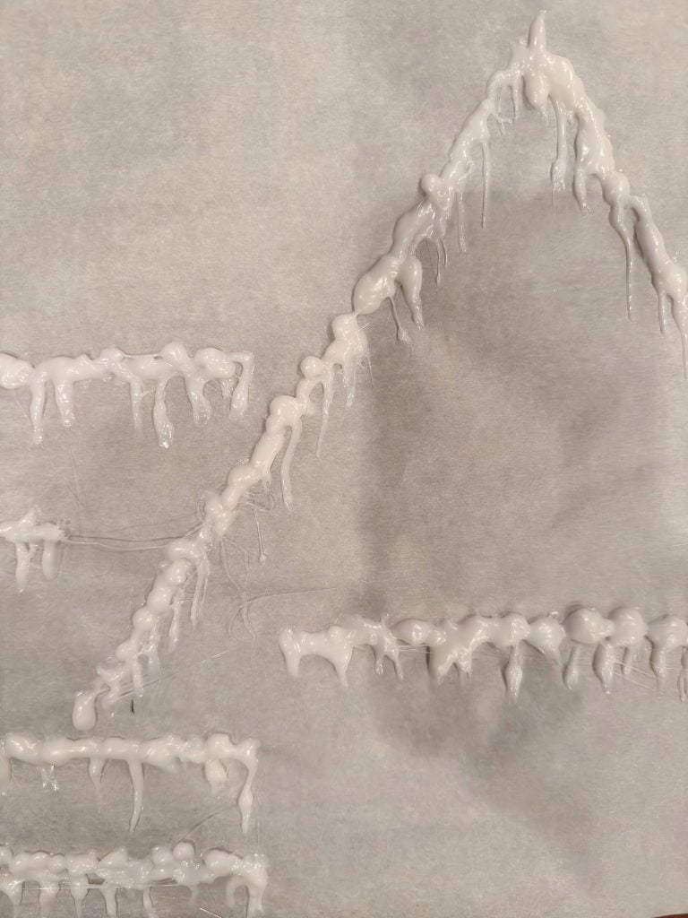 White glue is dripped in zigzag and triangular patterns on a sheet of parchment paper, forming textured raised lines.