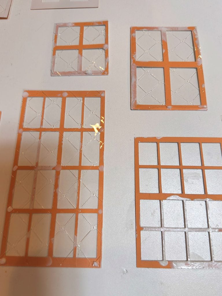 Several orange plastic grid templates with square cutouts are placed on a white surface. Some templates have diagonal lines inside the squares.