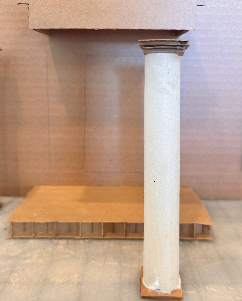 A cardboard model featuring a single column in front of a shallow stage with a rectangular outline on the backdrop.