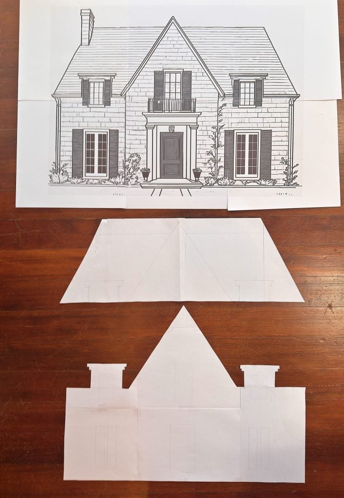 A drawing of a house facade is shown above two cut-out paper shapes with pencil sketches, all placed on a wooden surface.