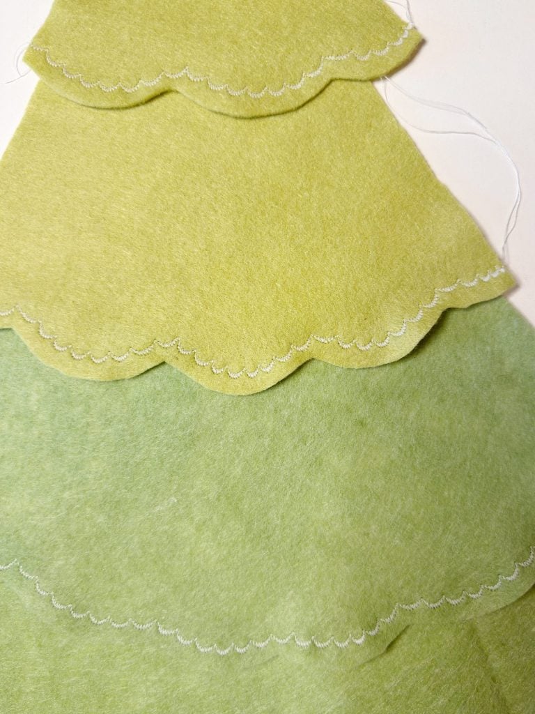 Three layers of green felt fabric with scalloped edges and visible stitching, arranged in a stacked pattern on a white surface.