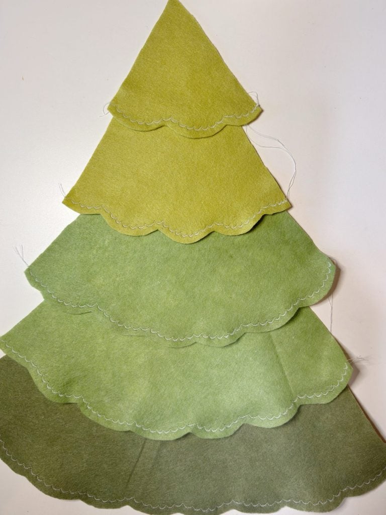 Four layers of green felt with scalloped edges are stacked in a tree shape, resembling a stylized Christmas tree, on a white background.