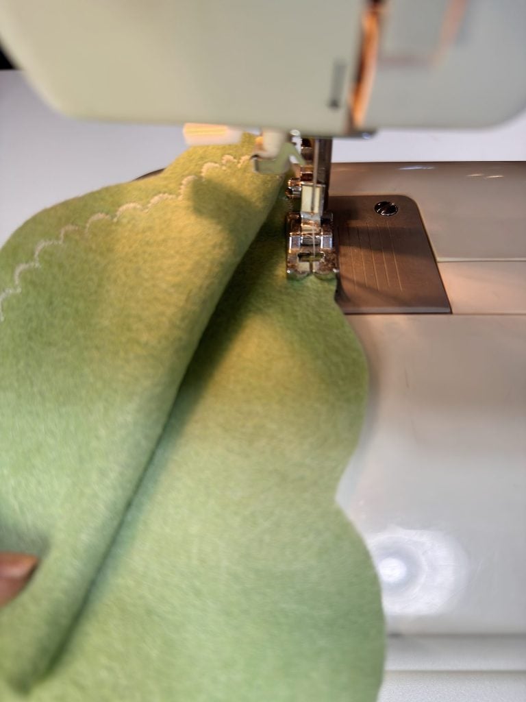 A close-up of light green fabric with a wavy stitched edge being sewn on a sewing machine.
