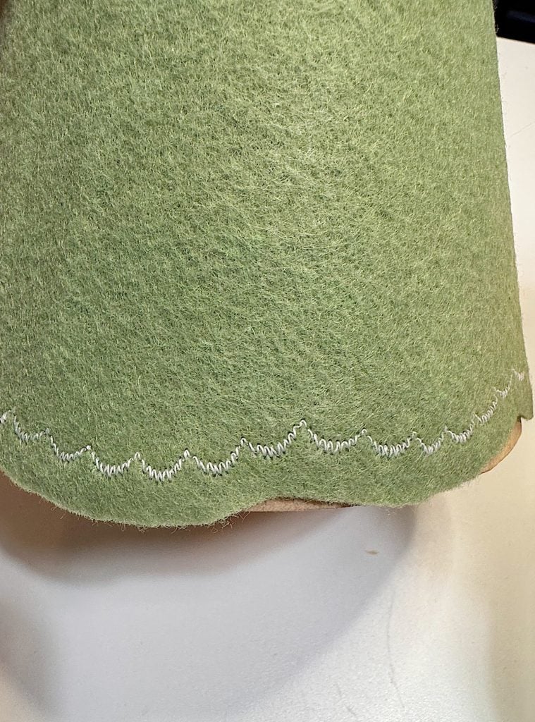 Close-up of green felt fabric with a decorative white zigzag stitch along the edge, placed on a white surface.