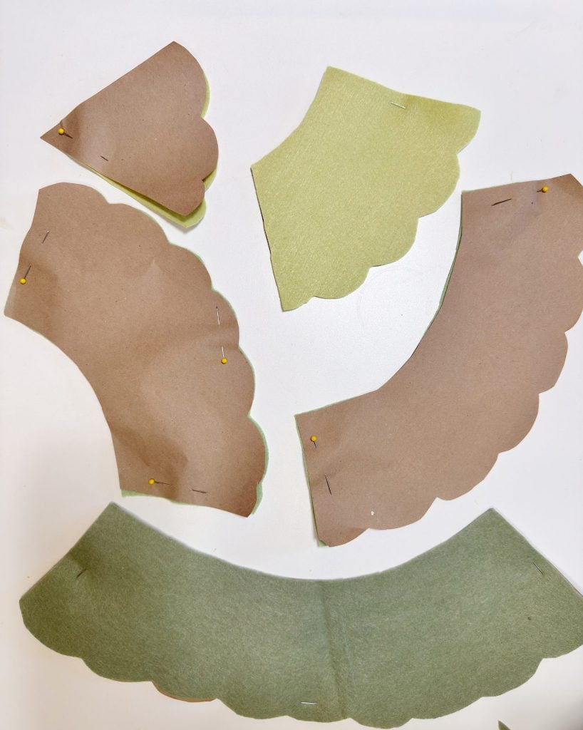 Several scalloped-edge fabric and paper pieces are pinned together and arranged on a white surface, likely as pattern pieces for a sewing project.