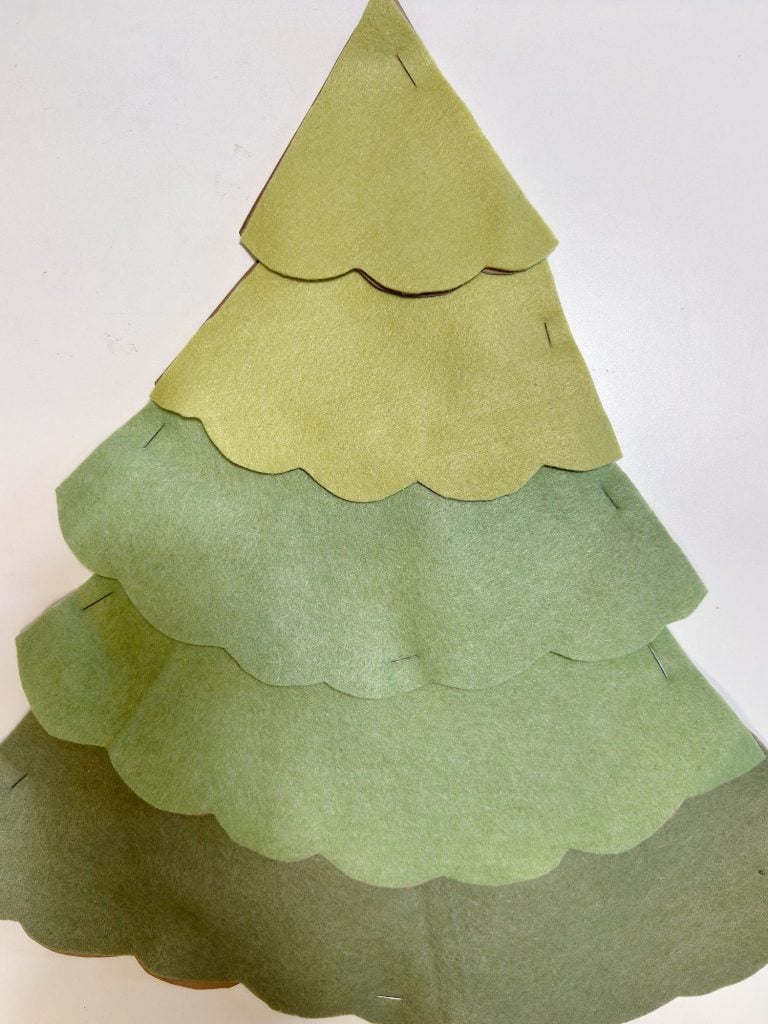 A handmade Christmas tree made of layered green felt pieces with scalloped edges, each shade of green getting darker toward the bottom, arranged on a white background.