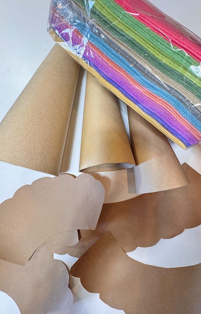 Brown paper cones, cut paper shapes, and a packaged stack of colorful felt sheets are arranged on a white surface.