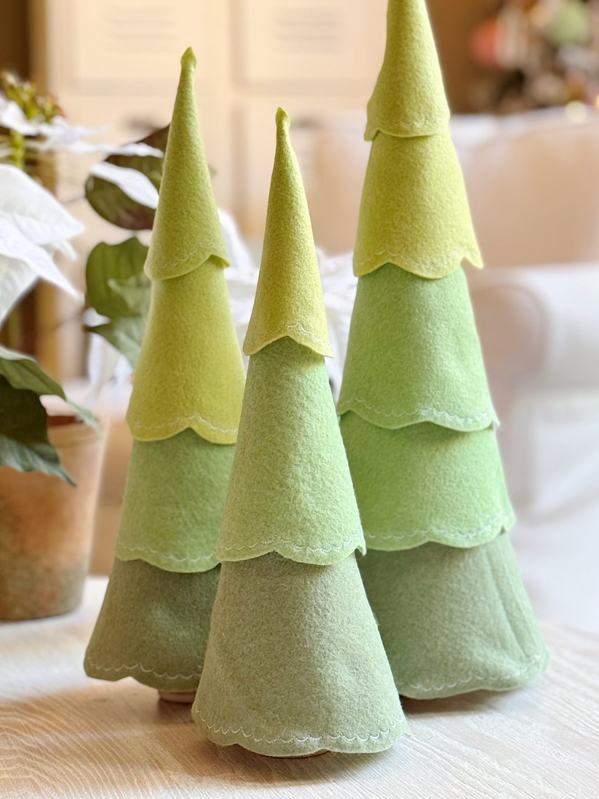 Three decorative felt trees in varying shades of green are arranged on a table in a softly lit indoor setting.
