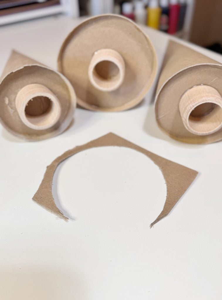 Three empty cardboard cones with the tops cut off are on a white surface, with a curved section of cardboard placed in front of them.