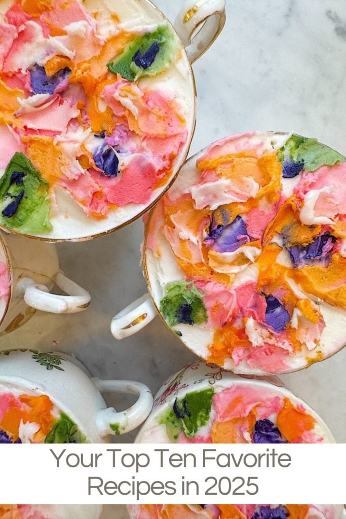 Several teacups filled with whipped, colorful, flower-themed desserts are arranged on a marble surface. Text below reads: "Your Top Ten Favorite Recipes in 2025.