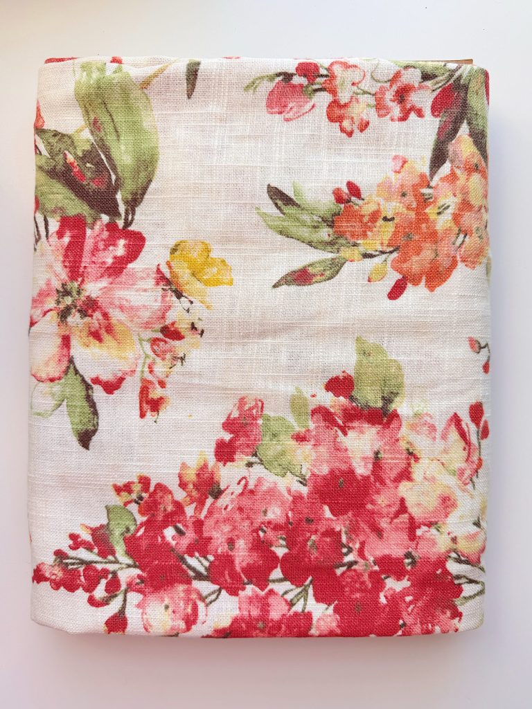 A folded piece of fabric with a floral pattern in red, pink, orange, and green on a white background.