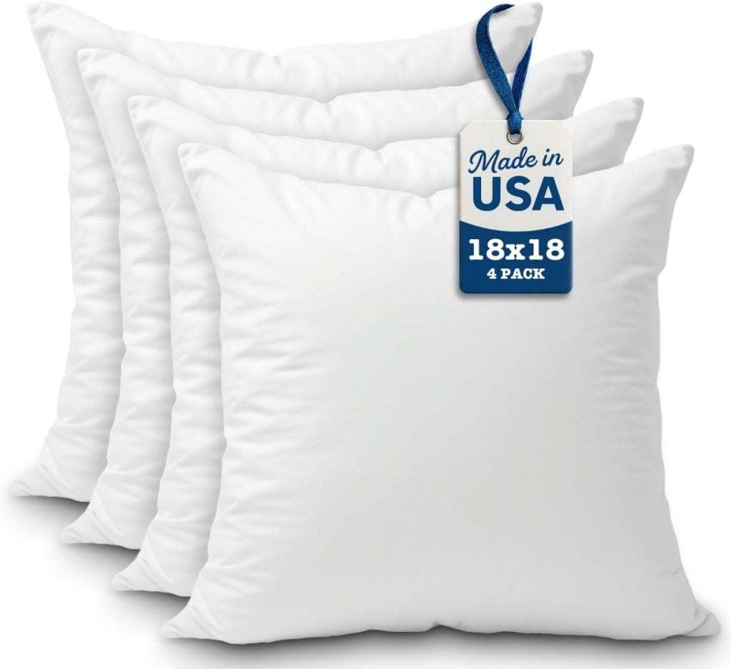 Four white square pillows are stacked with a tag reading "Made in USA, 18x18, 4 Pack" attached to the front pillow.