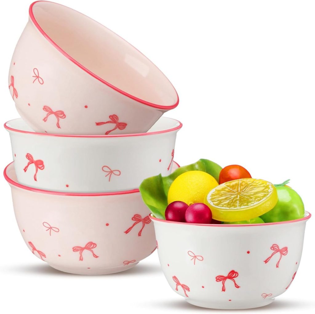 A set of four ceramic bowls with pink bow patterns, three stacked and one filled with assorted artificial fruits.