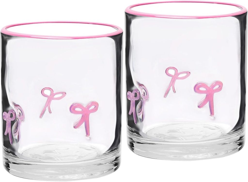 Two clear glass tumblers with pink rims and pink bow designs on the sides, placed side by side on a white background.