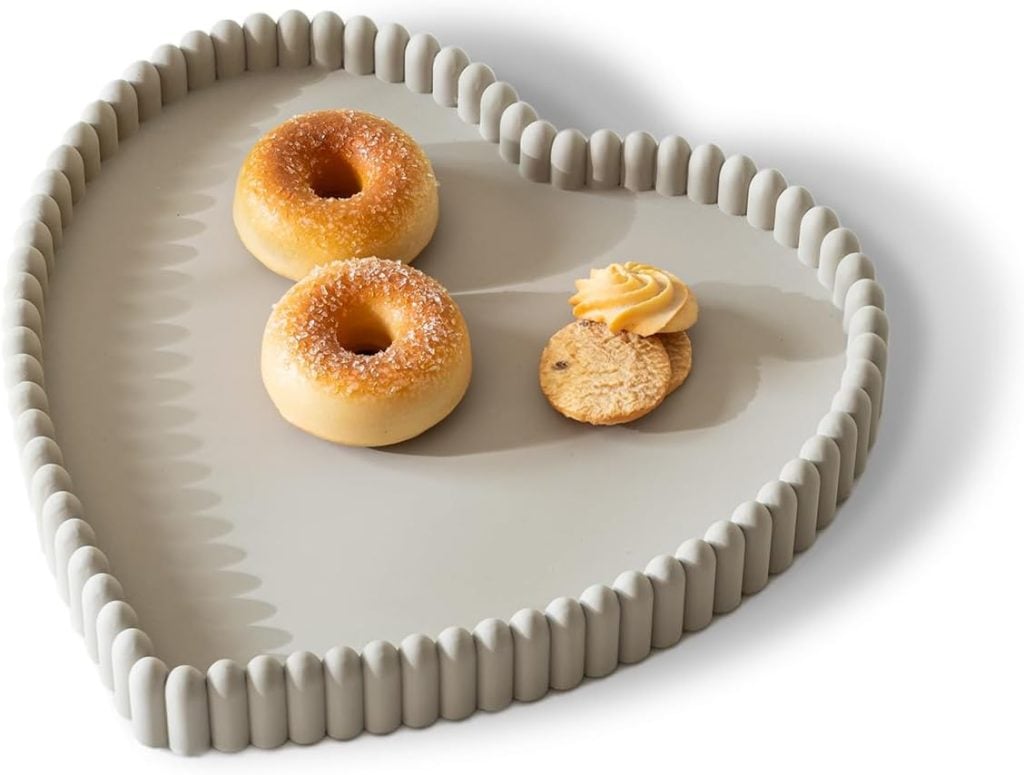 A heart-shaped, light gray tray holds two sugar-glazed donuts, a round cookie, and a small swirl of piped frosting.