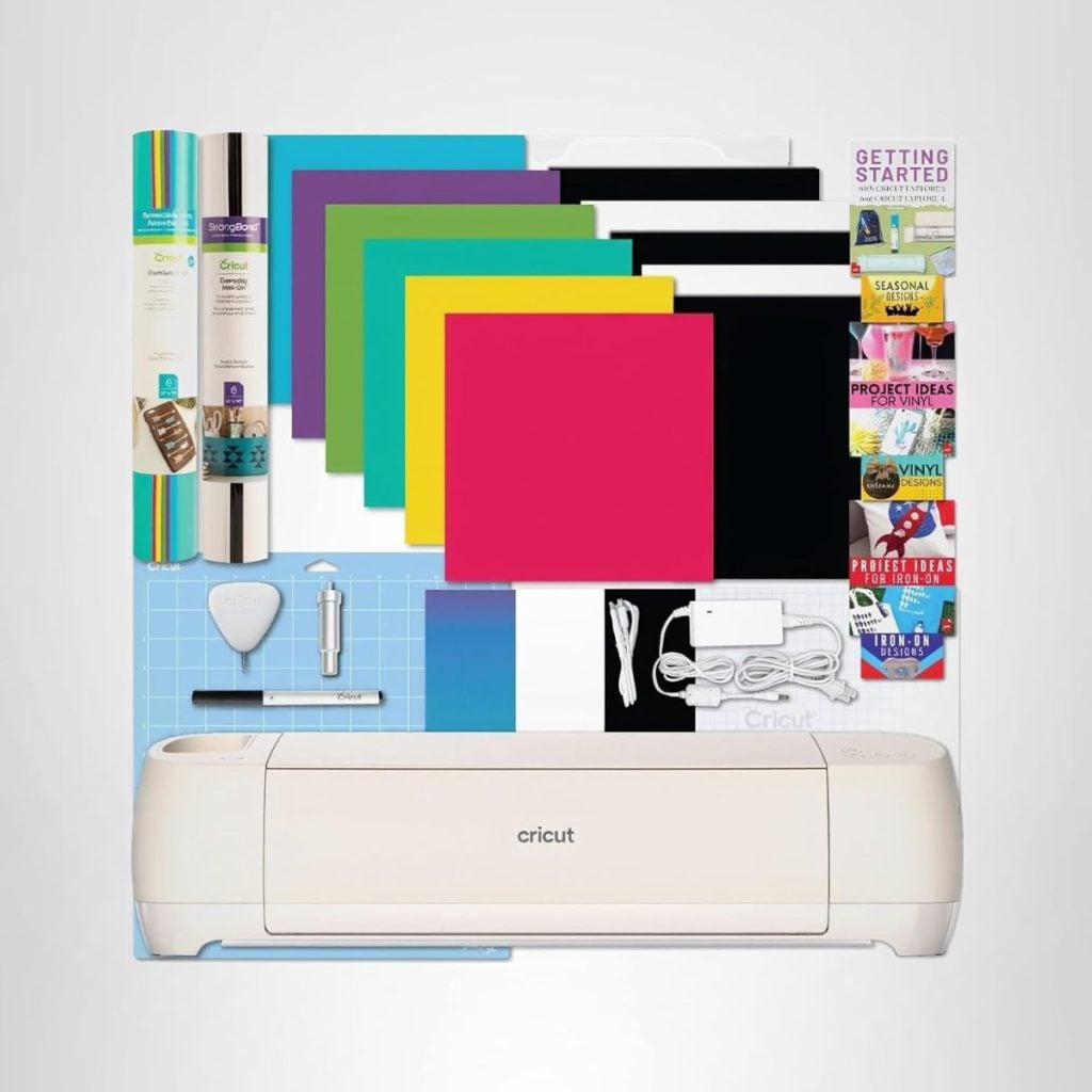 A Cricut cutting machine with assorted colored vinyl sheets, tools, cords, and instructional booklets arranged neatly on a white background.