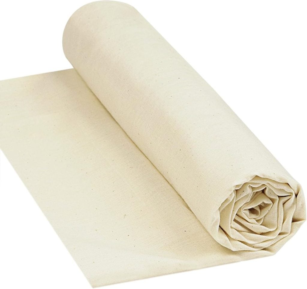 A large roll of plain, unbleached cotton fabric is partially unrolled on a flat surface.
