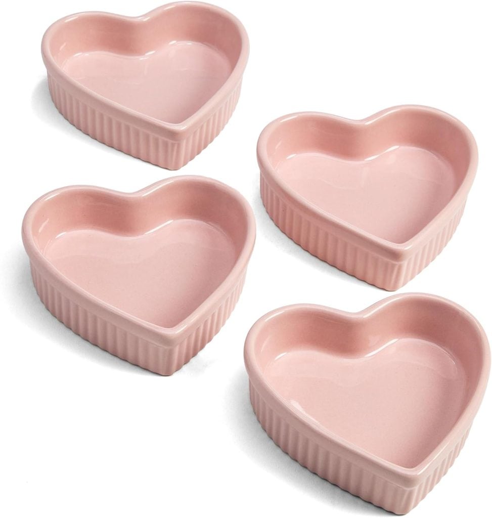 Four pink, heart-shaped ceramic ramekins are arranged on a white background.