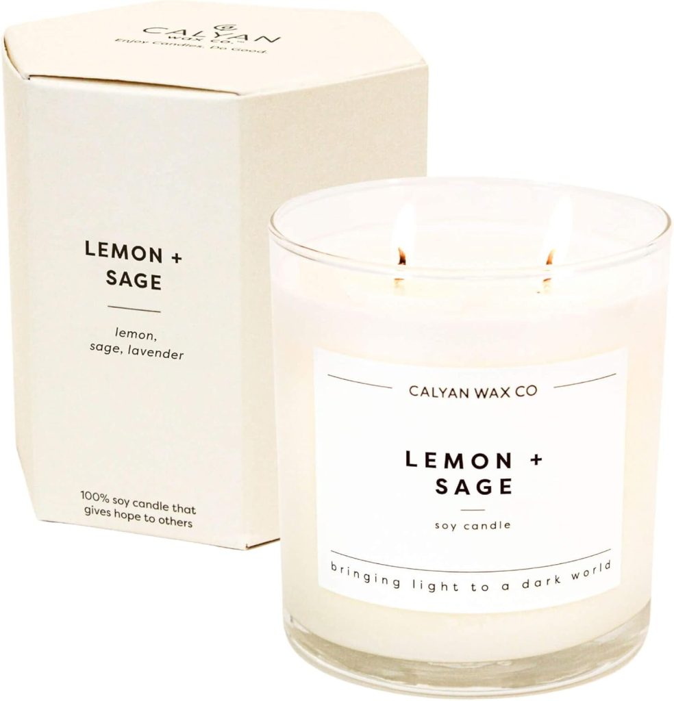 A glass jar soy candle labeled "Lemon + Sage" sits next to its matching box, both featuring minimalist white packaging with black text&mdash;an inviting addition to your Things To Do This Year list for relaxation and ambiance.