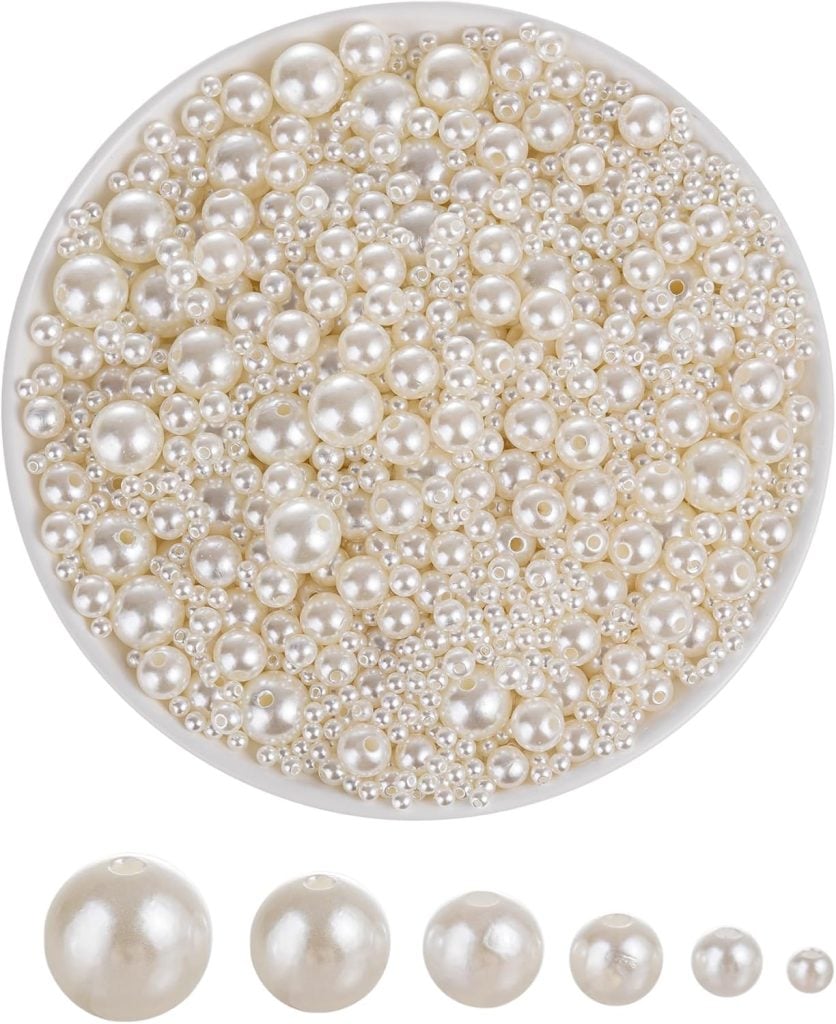A round container filled with assorted sizes of white pearls, with five individual pearls of varying sizes displayed below.